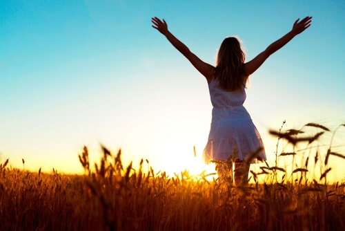 woman standing in a field, facing the sunrise, barefoot with arms outstretched to the sky representing hope, strength, and new beginnings